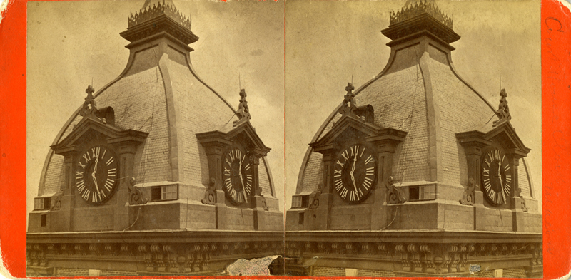 Black and white photo in sepia tones of two domes side by side. Each dome has two clocks with Roman numerals.