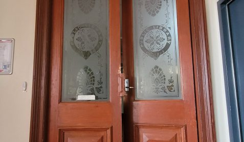 Large brown double doors. Glass in centre of panels has patterns etched in frosting and the words 'public library'