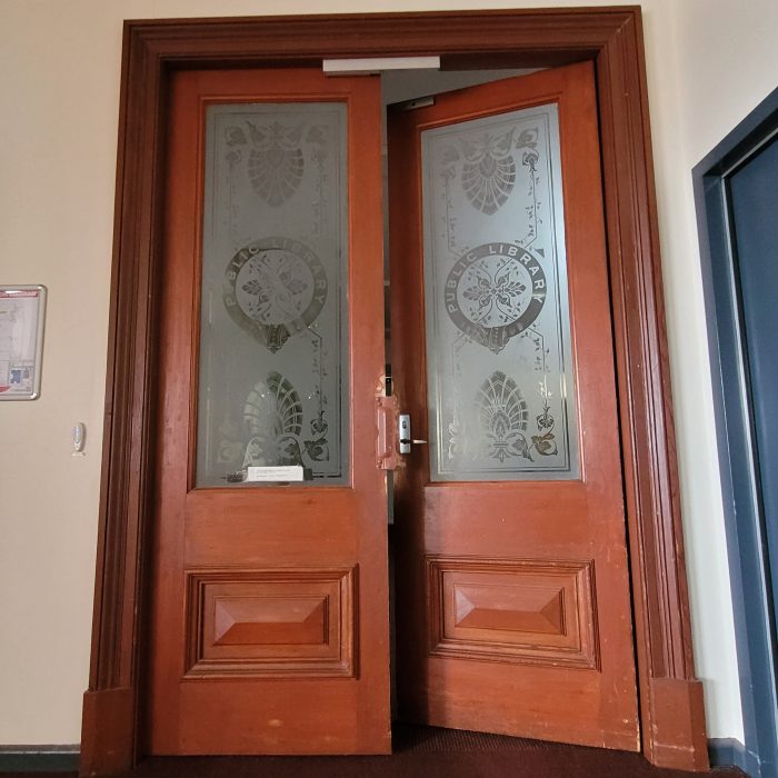 Large brown double doors. Glass panels have pattern and the words 'public library' etched in glass.